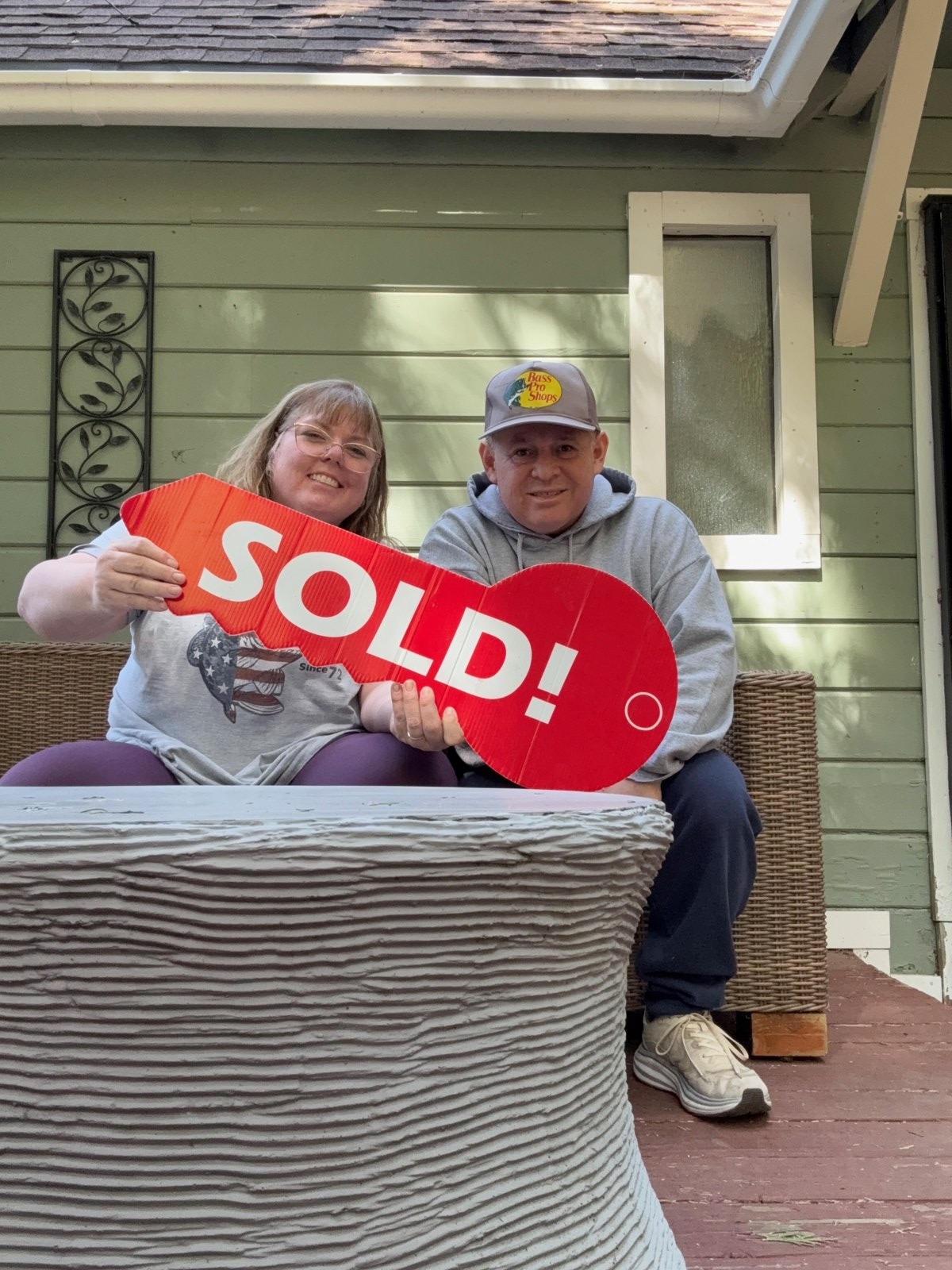 Happy homeowners holding a red SOLD key on their front porch